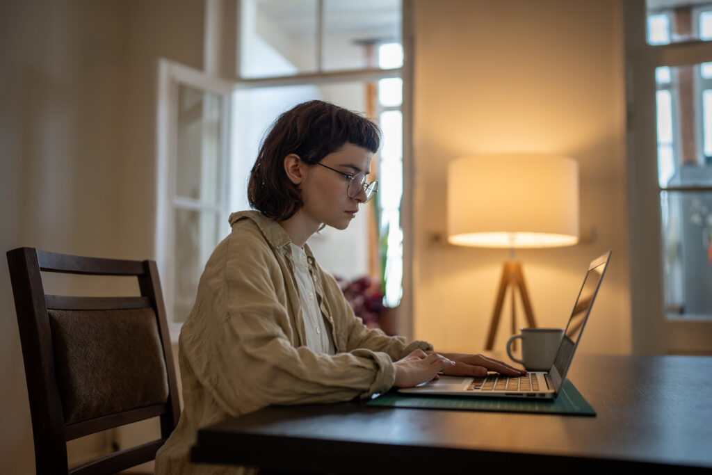 Eine junge Frau sitzt an einem Schreibtisch und schaut fokussiert und konzentriert auf ihren Laptop.